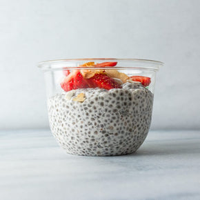 A clear plastic tub filled with coconut chia pudding topped with fresh strawberries.
