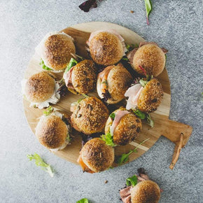 A selection of mini sourdough rolls with fillings like ham, beef, chicken, turkey or smoked salmon on a large round wooden board.