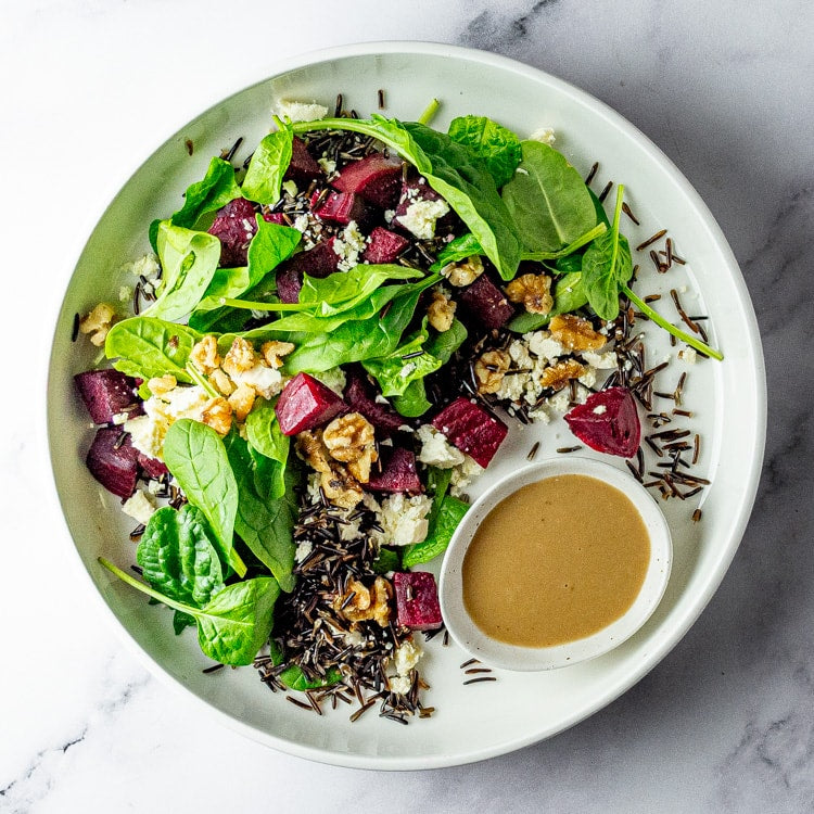 Plated salad with beetroot, walnut, feta, spinach and wild rice with dressing on a marble surface