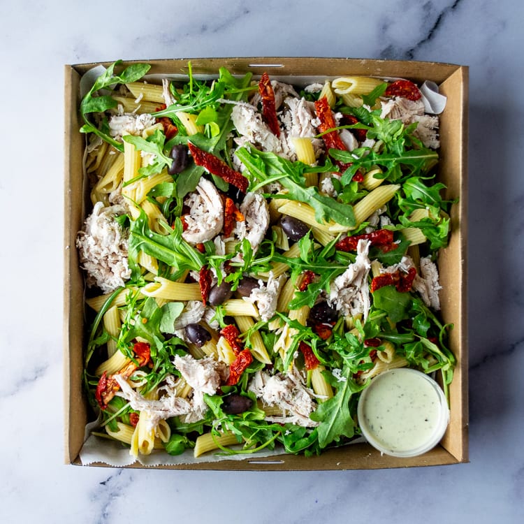 Box of salad with shredded chicken, penne, sun-dried tomatoes, kalamata olives, peppery rocket, and pesto mayonnaise