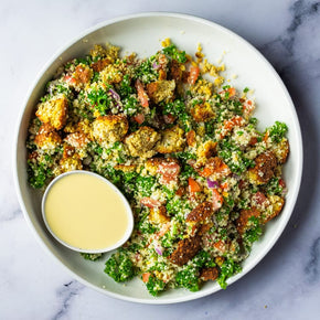 Falafel, quinoa, tomatoes, red onion, fresh parsley, and lemon vinaigrette in a large salad bowl on a marble table