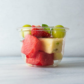 A clear plastic tub filled with mixed fruits including sliced strawberries, watermelon, grapes, and pineapple.