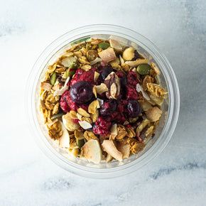 A top view of a granola tub with coconut yoghurt and berry compote, garnished with nuts and seeds.