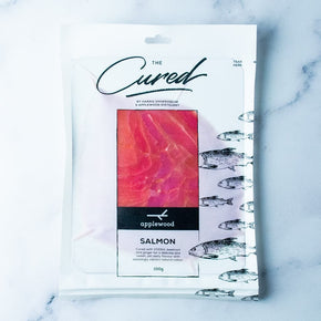 A 350g package of Harris Smokehouse Vodka, Beetroot & Ginger Cured Salmon in a clear plastic pouch with a white background, fish illustrations, and a central salmon fillet photo, photographed on a light marble surface.