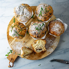 A wooden board with freshly baked muffins dusted in icing sugar.