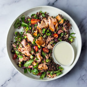 Miso salmon, mixed rice, cherry tomatoes, cucumber, red onion, pickled ginger, wasabi peas and wasabi mayo in a large salad bowl on a marble table