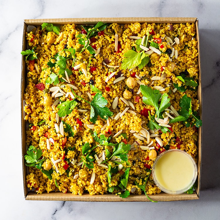 Box of moroccan couscous salad with greens and chickpeas on a marble surface