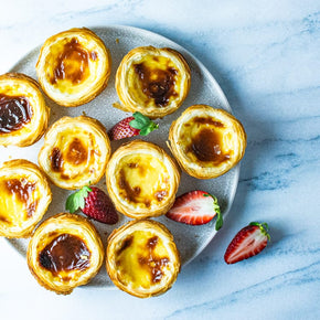 A large round plate with nine Portuguese custard tarts, garnished with strawberries on a marble table.