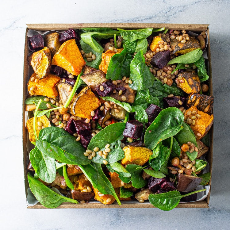 Box of salad with roasted vegetables and greens on a light background