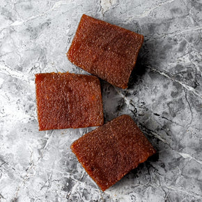 Three square blocks of quince paste arranged on a gray marbled surface.