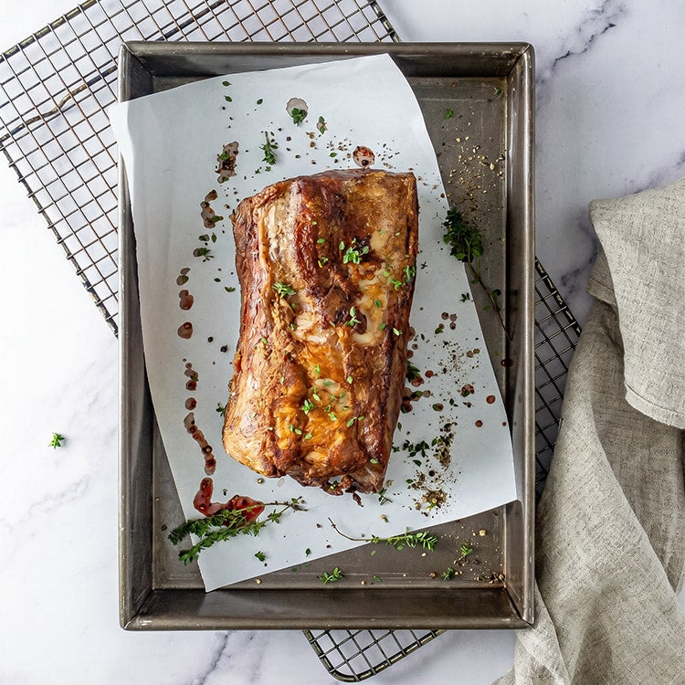 Roasted beef on a baking tray with herbs on a marble countertop