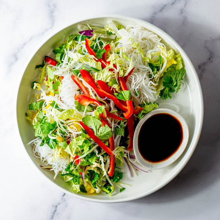 Salad with vermicelli noodles, cos, capsicum and bean sprouts with dressing in a cardboard box on a marble surface