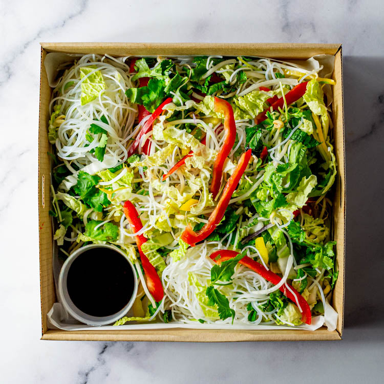 Salad with vermicelli noodles, cos, capsicum and bean sprouts with dressing in a cardboard box on a marble surface