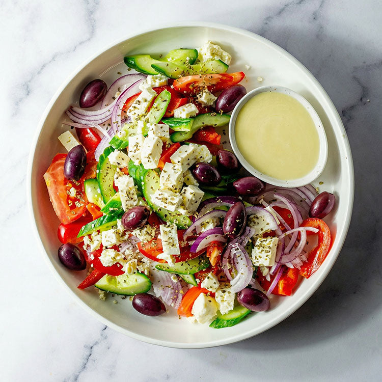 Platter of tomato, cucumber, red capsicum, olives, feta, red onion, oregano, and lemon vinaigrette on a marble surface