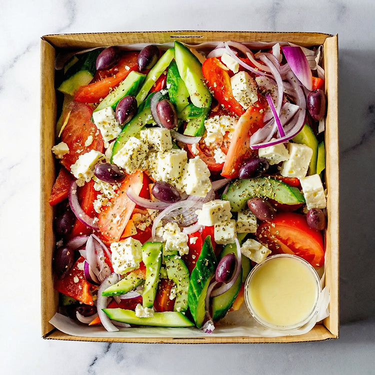 Box of tomato, cucumber, red capsicum, olives, feta, red onion, oregano, and lemon vinaigrette on a marble surface