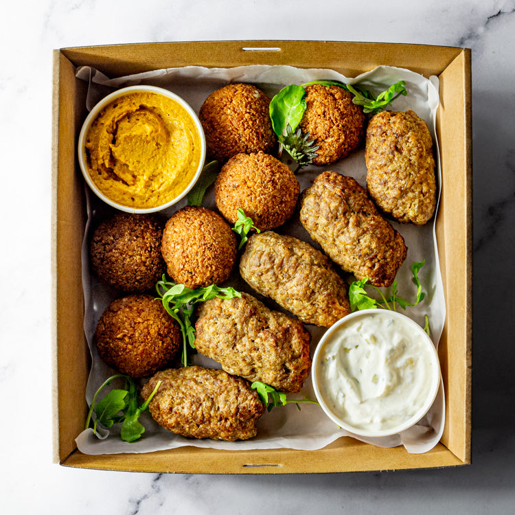 Box of lamb kofta, falafel, pumpkin hummus and tzatziki on a marble surface