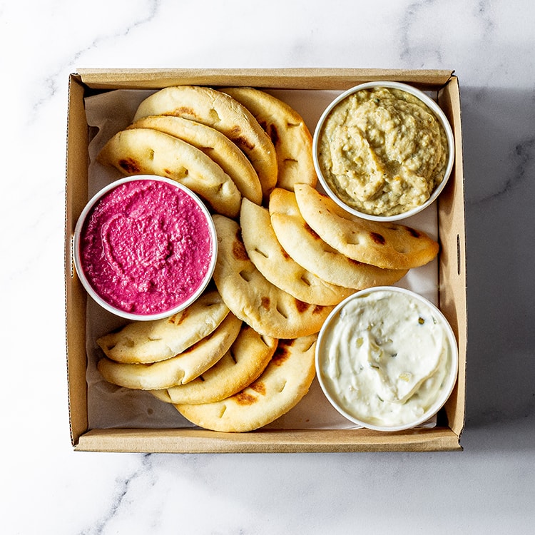 Box of pita bread with three dips on a marble surface