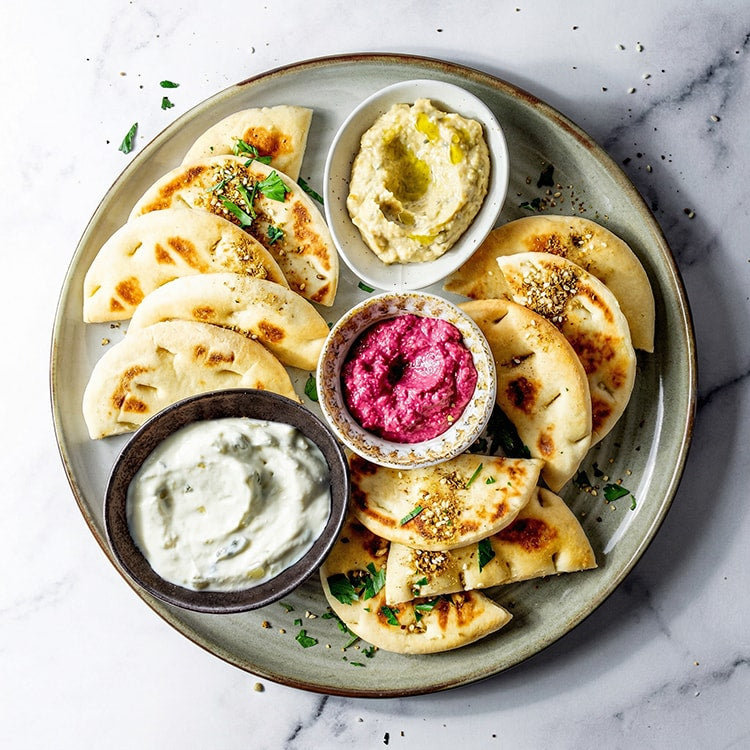 Platter of flatbreads with various dips on a marble surface