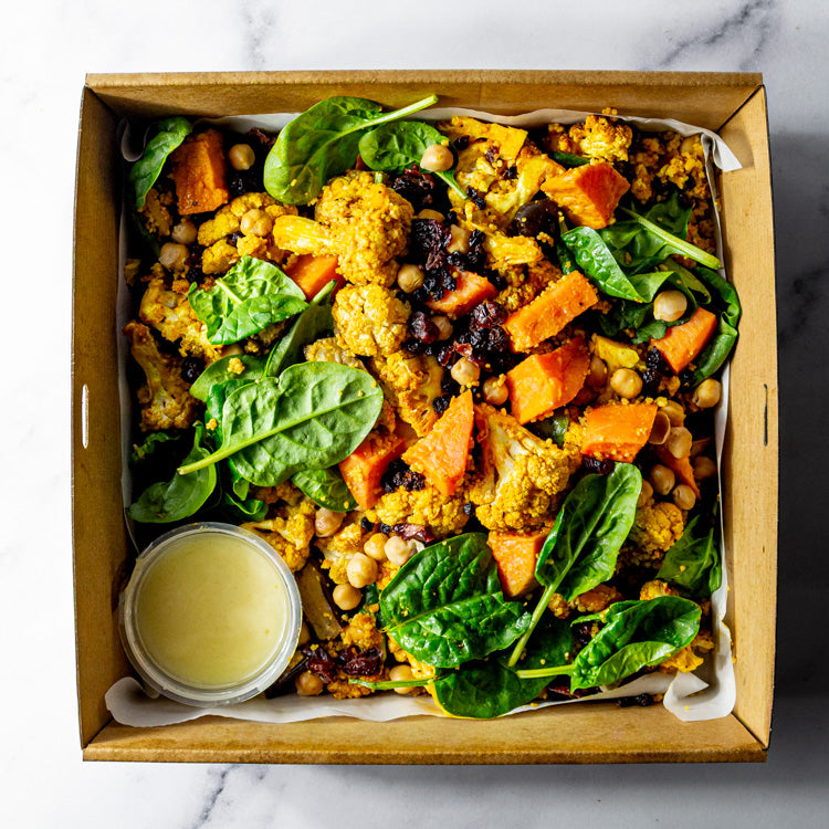Platter of Moroccan spiced cauliflower, sweet potato, eggplant, chickpeas, baby spinach, cranberries, and currants with bowl of lemon saffron vinaigrette on a marble surface