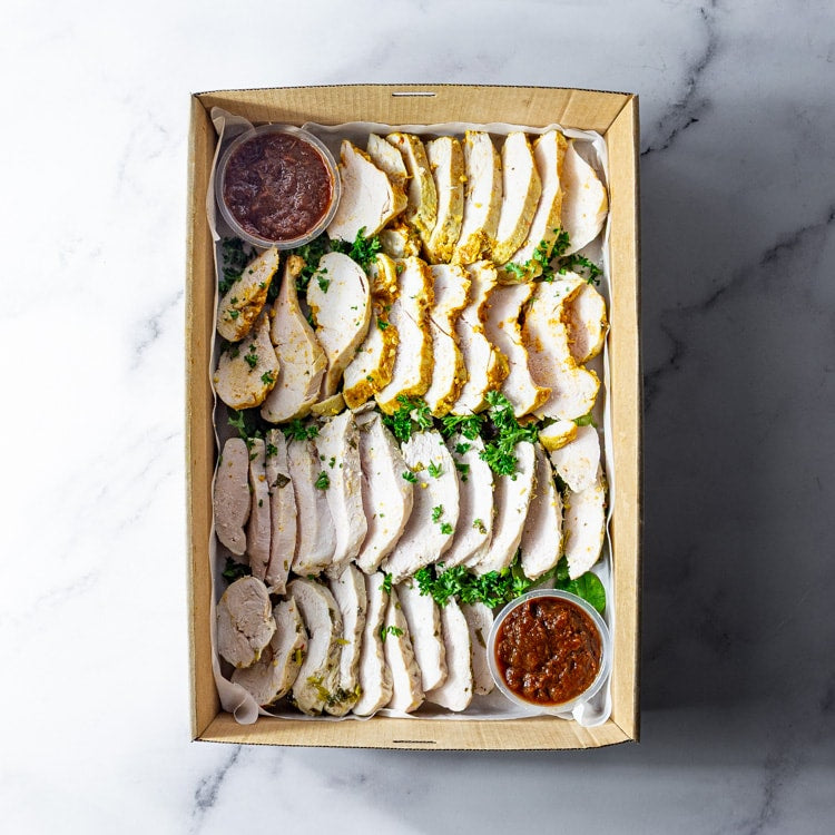 Box of sliced chicken with sauce and garnishes in a box on a marble surface