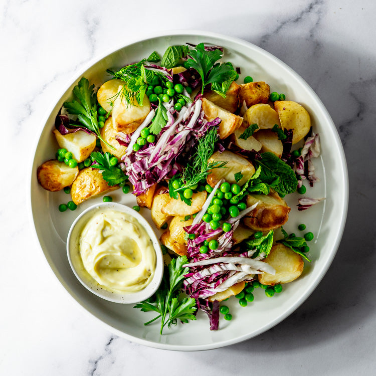Platter of potato, peas, dill, parsley, and baby spinach with honey seeded mustard mayonnaise on a marble surface