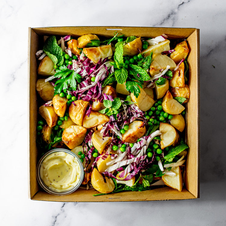 Platter of potato, peas, dill, parsley, and baby spinach with honey seeded mustard mayonnaise on a marble surface