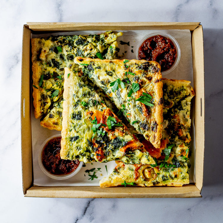 Slices of spinach, creamy feta and sun dried tomato tart in a box on a marble surface