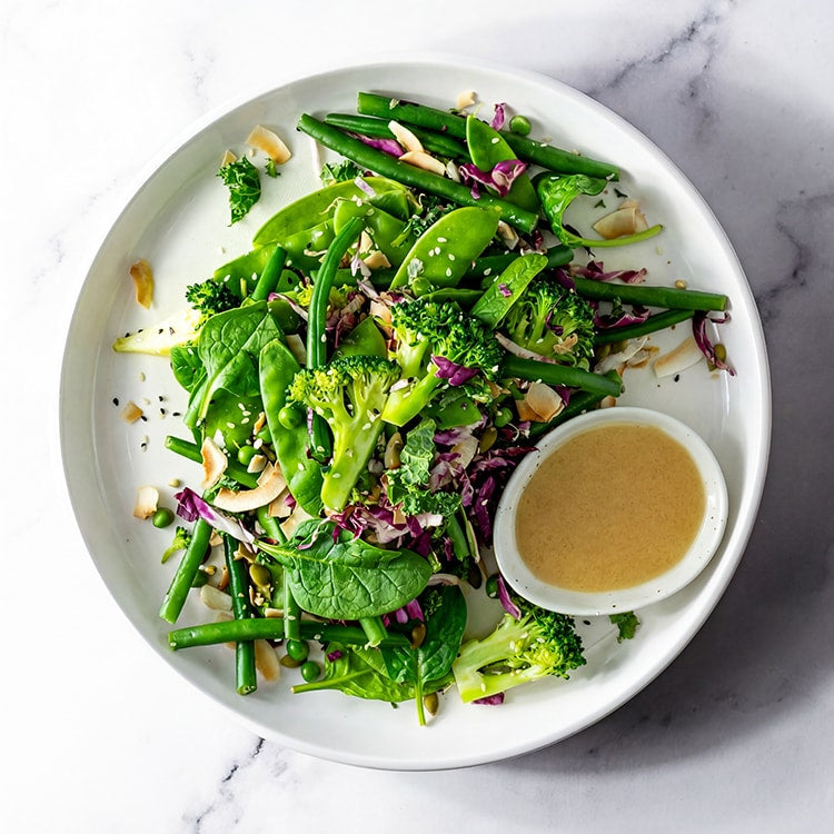 Green salad with a small bowl of dressing on a white plate, set against a marble background.
