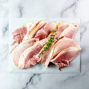 Sliced ham arranged on a white rectangular board, garnished with thyme sprig, set on a light marble surface.