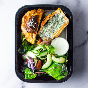 A rsmall ectangular container with vegetarian frittata, garden salad, tomato relish and balsamic dressing on a marble table.