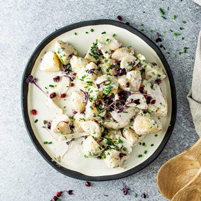 A large round white plate with a mix of steamed chat potatoes, fennel, and chives, with a small bowl of horseradish mayonnaise on a marble table.