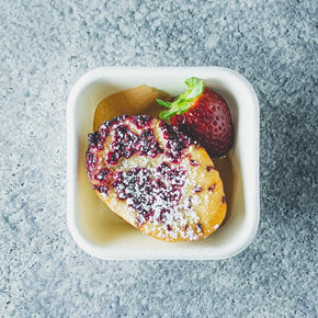 A single friand and strawberry in a small container.