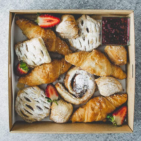 A box of pastries including croissants, danishes, strawberries and jam.