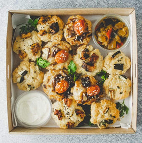A square box filled with 12 savoury mini muffins in a mix of two flavours with tubs of relish and sour cream on a marble table.