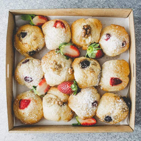 A box of mini sweet muffins with a strawberry garnish, dusted with powdered sugar.