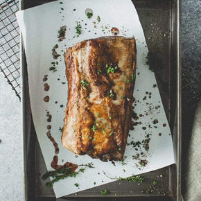 A whole seasoned rib eye fillet on a piece of parchment paper, garnished with herbs, on a baking tray.