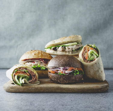 Side view of an assortment of rolls and wraps with a mix of fillings, displayed on a wooden board.