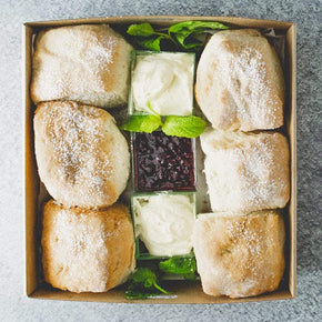 A box of freshly baked scones served with jam and cream, garnished with mint leaves.