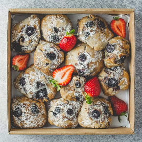 A box of vegan mini sweet muffins topped with powdered sugar and accompanied by sliced strawberries.